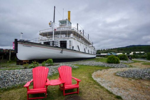 a white sternwheeler boat in background with two red ainadrok chairs in the foregound