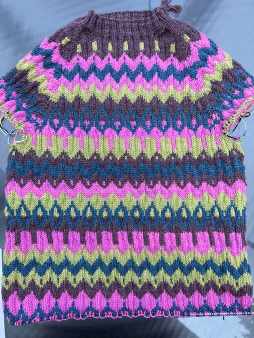 This is a photo of a sweater being knitted that is still under construction. It is multi-coloured.